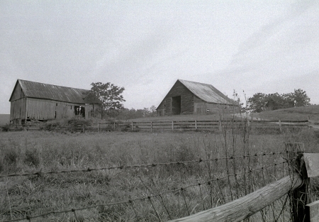 A photograph of two old barns on a farm including a rustic wire fence.